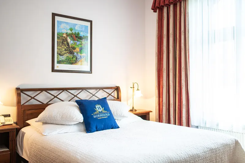 Cama junto a una ventana con cortinas — Deluxe, Hornigold